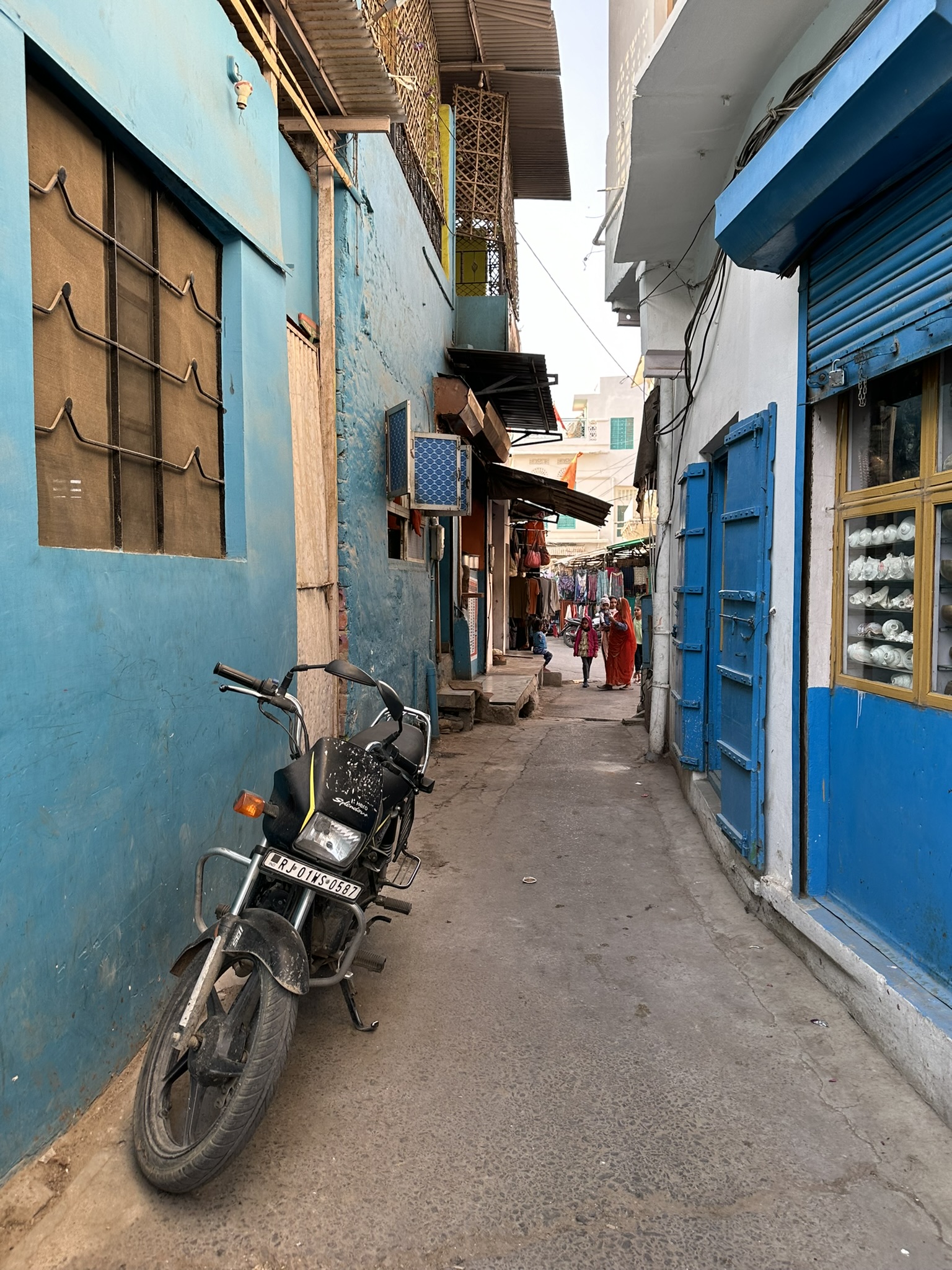 Wąska uliczka Jodhpur z niebieskimi domami, motocyklem i sklepami w tle