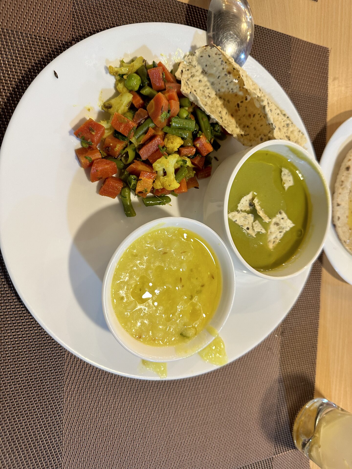 Talerz pełen indyjskich potraw: warzywa curry, dwie zupy, papadum na białym talerzu.